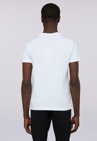 Bílý bavlněný tričko s krátkým rukávem, kulatým výstřihem a jednoduchým designem, viděno zezadu na neutrálním pozadí.