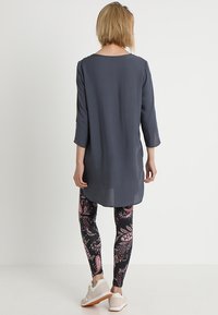 Szara tunika z okrągłym dekoltem, z rękawami 3/4. Zestawiona z czarnymi legginsami w paisley w kolorze różowym i białym. Beżowe buty.