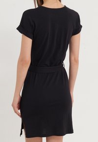 Czarna sukienka z krótkim rękawem wykonana z miękkiego materiału, z dopasowaną talią i bocznymi rozcięciami dla urozmaicenia. Minimalistyczny design z okrągłym dekoltem.