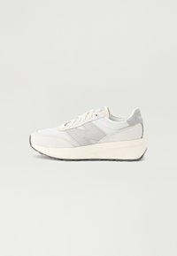 Vit sportig sneakers med en slät tygöverdel, ljusgrå accenter och en kraftig vit mellansula. Har runda snören och en texturerad gummisula.