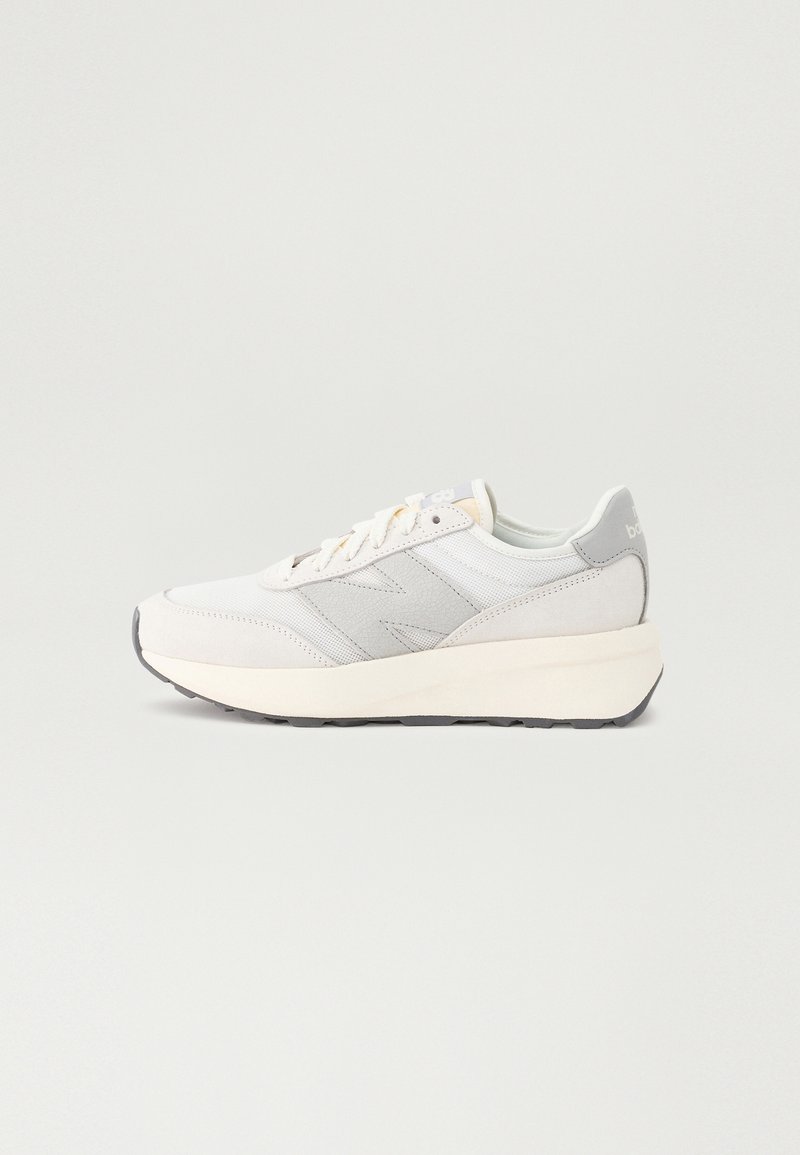 Vit sportig sneakers med en slät tygöverdel, ljusgrå accenter och en kraftig vit mellansula. Har runda snören och en texturerad gummisula.