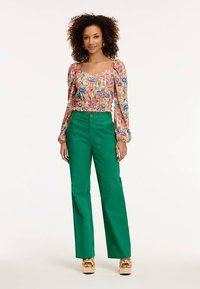 Farebná kvetinová blúzka s nafúknutými rukávmi, zoštíhleným pásom a zelené široké nohavice. Dokončené zlatými sandálmi na platforme.