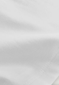 Hvidt stof med en glat tekstur, der viser et fint, ensartet væv og synlige sømme langs kanten. Blødt og let udseende.