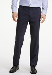 Marineblauwe kledingbroek met een getailleerde pasvorm, rechte voorkant en een gladde textuur, gecombineerd met zwarte dresschoenen. Strakke lijnen en geen zichtbare patronen.