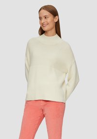 Kremowy sweter z dzianiny z wysokim kołnierzem, z teksturowanym wzorem i luźnym krojem. W połączeniu z jasnoróżowymi spodniami z wysokiej jakości kordurowej tkaniny.