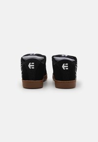 Schwarze Skate-Schuhe mit strukturiertem Rücken, weißen Logo-Akzenten und einer braunen Gummisohle. Das Netzfutter sorgt für Atmungsaktivität.