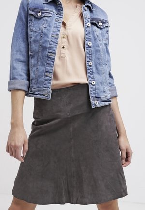 Veste en denim bleu clair avec des détails usés, assortie à un haut beige et une jupe évasée en daim gris avec des coutures et une texture lisse.