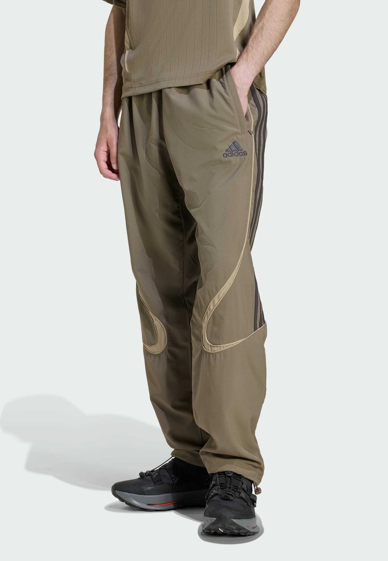 Olivovo zelené teplákové nohavice so zúženým strihom, s kontrastnými čiernymi pruhmi a zakrivenými švami. Vyrobené z ľahkého, hladkého materiálu.