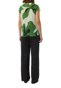 Vihreä ja valkoinen neulepaita, jossa on abstrakteja lehtikuoseja; lyhyet hihat, pyöreä kaula-aukko ja rento malli, yhdistetty mustiin leveisiin housuihin.