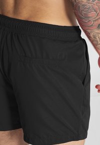 Bañador negro con cintura elástica y un bolsillo trasero, fabricado en un tejido ligero y suave con un acabado mate.