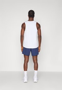 Biały bezrękawnik sportowy, granatowe szorty, białe buty sportowe i skarpetki do kostek. Prosty, dopasowany krój z gładką teksturą.