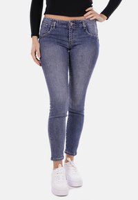 Jeans skinny in denim con una lavatura blu media, dotati di cinque tasche, una zip frontale e chiusura con bottone, abbinati a sneakers bianche.