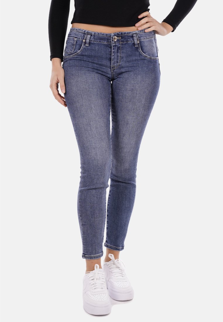 Jeans skinny in denim con una lavatura blu media, dotati di cinque tasche, una zip frontale e chiusura con bottone, abbinati a sneakers bianche.