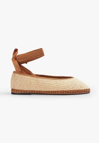 Scarpa piatta con tomaia intrecciata color tan, punta affusolata e cinturino marrone alla caviglia. Presenta una suola in sughero testurizzata con dettagli di bordatura cucita.