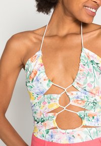 Top halter com padrão floral em tecido leve. Apresenta um decote profundo, laterais franzidas e costas entrelaçadas com alças brancas.