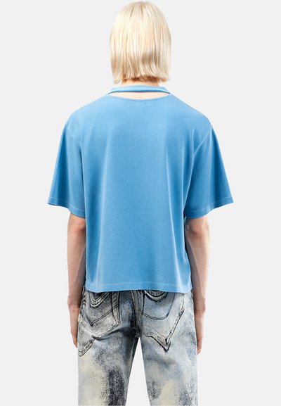 Lichtblauwe katoenen t-shirt met korte mouwen en een cropped ontwerp, met een subtiele uitsnijding aan de achterkant. Gepaard met vervaagde jeans.