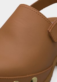 Κοντινό πλάνο καφέ δερμάτινου ξύστρου με ραμμένο επάνω μέρος και μεταλλικά καρφιά κατά μήκος της πλευράς.