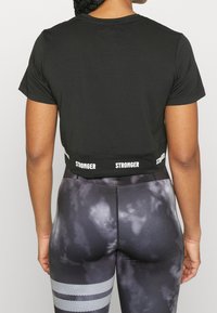 Camiseta corta negra con "STRONGER" impreso en blanco a lo largo del dobladillo, combinada con leggings de cintura alta que presentan un patrón de nubes grises y franjas reflectantes.