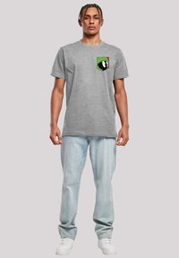 Grå bomull T-skjorte med rund hals, med et fargerikt tegneseriefigur lomme-design. Kombinert med lyseblå jeans og hvite sneakers.