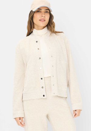 Beige snap-front jacket made of textured fabric, featuring two front pockets and a relaxed fit, paired with a matching top and pants.