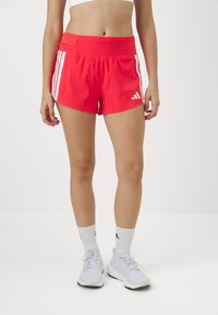 Pantalones cortos deportivos rojos hechos de un tejido ligero, con una cintura ancha, tres rayas blancas a cada lado y un pequeño logo.