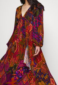 Lang, flydende kjole i livlige multicolor mønstre med dyb V-udskæring, lange ærmer og struktureret stof med blomster- og abstrakte designs.