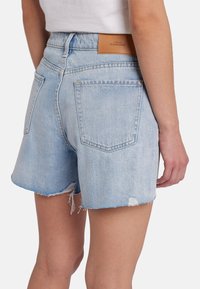 Shorts di jeans azzurro chiaro con orlo sfrangiato, due tasche posteriori e un'etichetta in pelle marrone sulla vita.