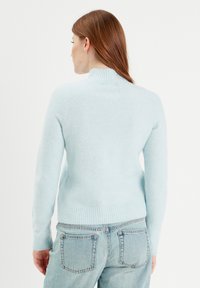 Lysblå sweater med ribbet hals og kant. Lavet af et blødt materiale, har den lange ærmer og et tætsiddende design, stylet med denim jeans.