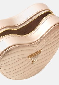 Goudkleurige, met rits afsluitbare tas in hartvorm met een doorgestikte textuur, gemaakt van lichtroze synthetisch materiaal, met een logo-accent aan de voorkant.