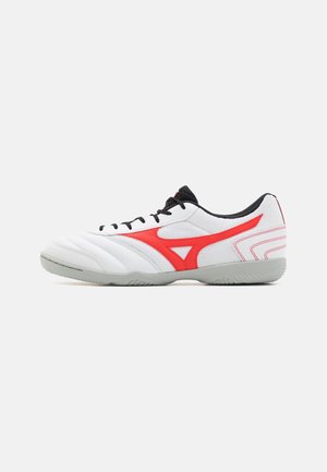 Weißer und grauer Sportschuh mit schwarzen Schnürsenkeln und rotem Logodetail an der Seite, konzipiert für Indoor-Aktivitäten.
