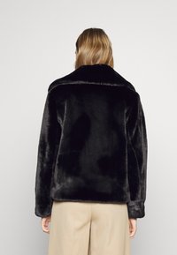 Sort imiteret pelsjakke med bred krave og lange ærmer. Blød tekstur, afslappet pasform og uden synlige lukninger eller mønstre.