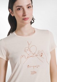 Kremowa koszulka z miękkiego materiału, z minimalistycznym wzorem wykonanym linią przedstawiającym dwie dłonie tworzące serce oraz tekstem „Re-pose.”