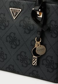 Sac à main en cuir noir texturé avec motif gaufré, ferrures dorées et porte-clés comportant des étiquettes rondes et rectangulaires gravées "GUESS".