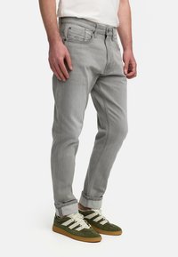 Grå denimjeans med lige pasform, fem lommer, knaplukning og opsmøg; parret med grønne og hvide sneakers.