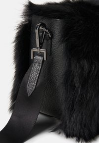 Sort taske med en kombination af læder og imiteret pels, en struktureret overflade og en aftagelig rem med en sikker lås.