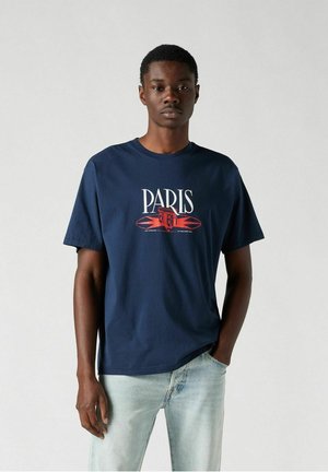 Navy blue t-shirt made of cotton, featuring a graphic print of a building with the text "PARIS" in red and white, round neck design.