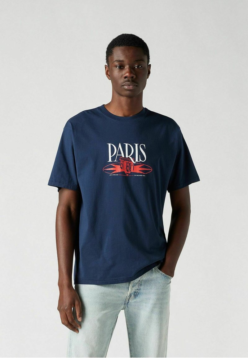 Camiseta de color azul marino hecha de algodón, con un estampado gráfico de un edificio y el texto "PARÍS" en rojo y blanco, diseño de cuello redondo.