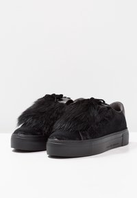 Schwarze Sneaker mit einem Obermaterial aus strukturierter Stoff und Fake-Fur-Akzenten. Rundliche Zehenpartie, flache Gummisohle und Schnürdesign.