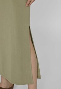 Vestido verde oliva de longitud a la rodilla, hecho de una tela suave, con una abertura lateral y un dobladillo recto. Diseño minimalista con líneas limpias.