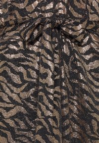 Svart och guld paljetttyg med ett mönster av tigerränder, med en texturerad yta och samlad detalj i mitten.