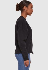 Black sweatshirt with a relaxed fit, round neckline, and ribbed cuffs. Detailed with a drawstring at the hem and soft cotton fabric.