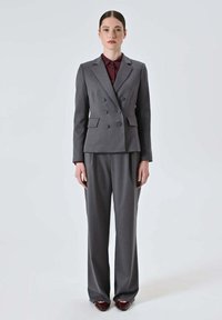Blazer doppiopetto grigio con pantaloni a gamba larga abbinati, realizzati in tessuto liscio. Presenta bottoni decorativi e una vestibilità sartoriale.