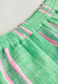 Tissu vert avec des rayures verticales roses et blanches ; présente une taille élastique froncée ; texture lisse, matériau léger.