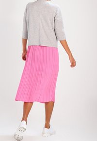 Gray cropped sweater with three-quarter sleeves paired with a pink pleated midi skirt. White sneakers complete the outfit.