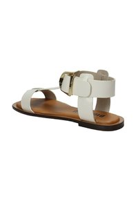 Sandal in pelle bianca con suola piatta marrone, dotata di una fascia larga e di un accento con fibbia in tonalità oro sul lato.