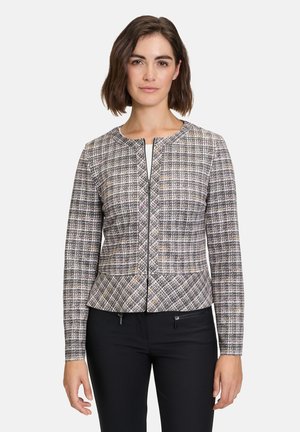 Veste en tweed texturé et multicolore avec un col rond, fermeture éclair sur le devant et coupe ajustée, associée à un pantalon noir slim.