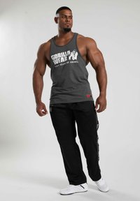 Pilkas maikutė su užrašu "GORILLA WEAR JUNGTINĖS AMERIKOS VALSTIJOS" baltu šriftu. Juodos sportinės kelnės su baltais šoniniu akcentais. Baltos batai.