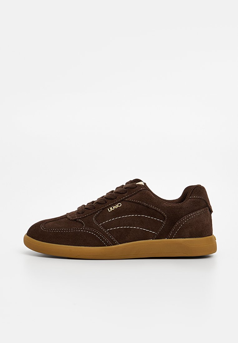 Brązowe zamszowe sneakersy z gumową podeszwą, zakrzywionymi białymi detalami przeszycia i zapięciem na sznurówki. Z logo po boku.