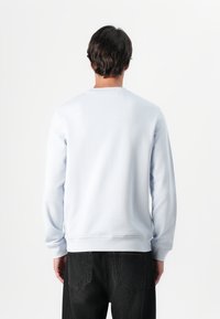 Sudadera azul clara de tejido suave con mangas largas y puños acanalados, combinada con jeans de mezclilla oscura, vista desde atrás.