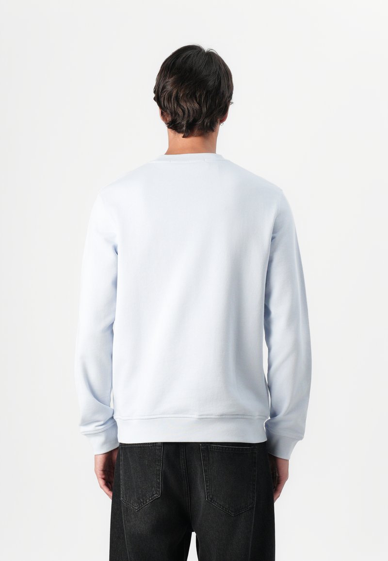 Un sweat-shirt bleu clair en tissu doux avec des manches longues et des poignets côtelés, associé à un jean en denim foncé, vu de l'arrière.
